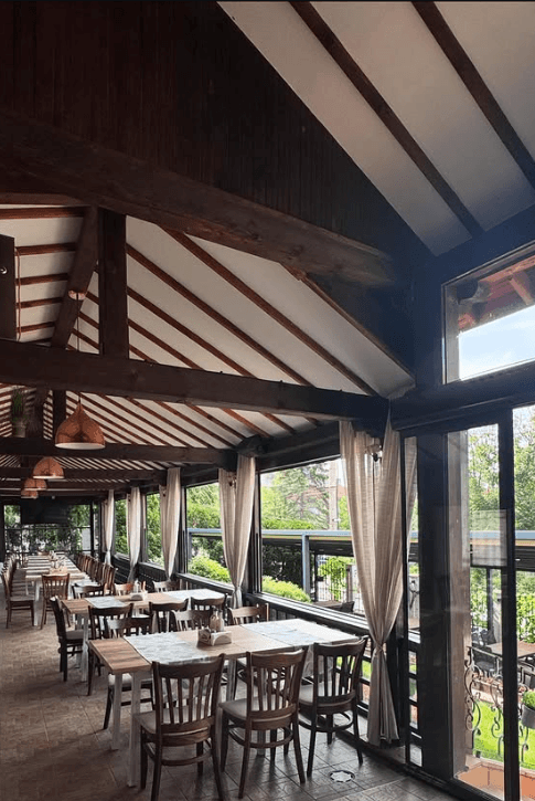 Covered terrace dining hall with wooden beams and long tables set for guests